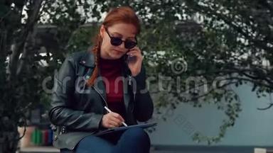 戴墨镜的年轻女子<strong>坐在公园里</strong>的长凳上，一边用手机说话，一边记录着在<strong>公园里</strong>的谈话